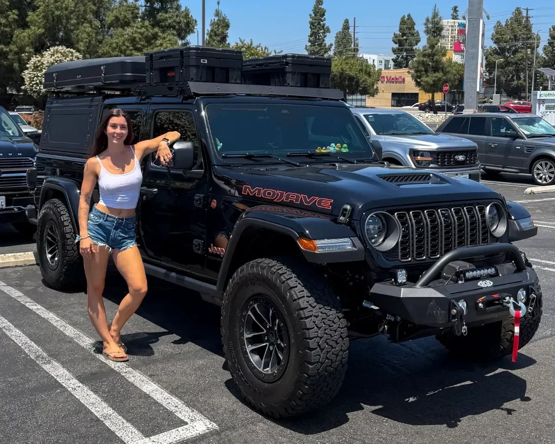 Emma Sinclair beside her black Jeep Gladiator with rooftop tent