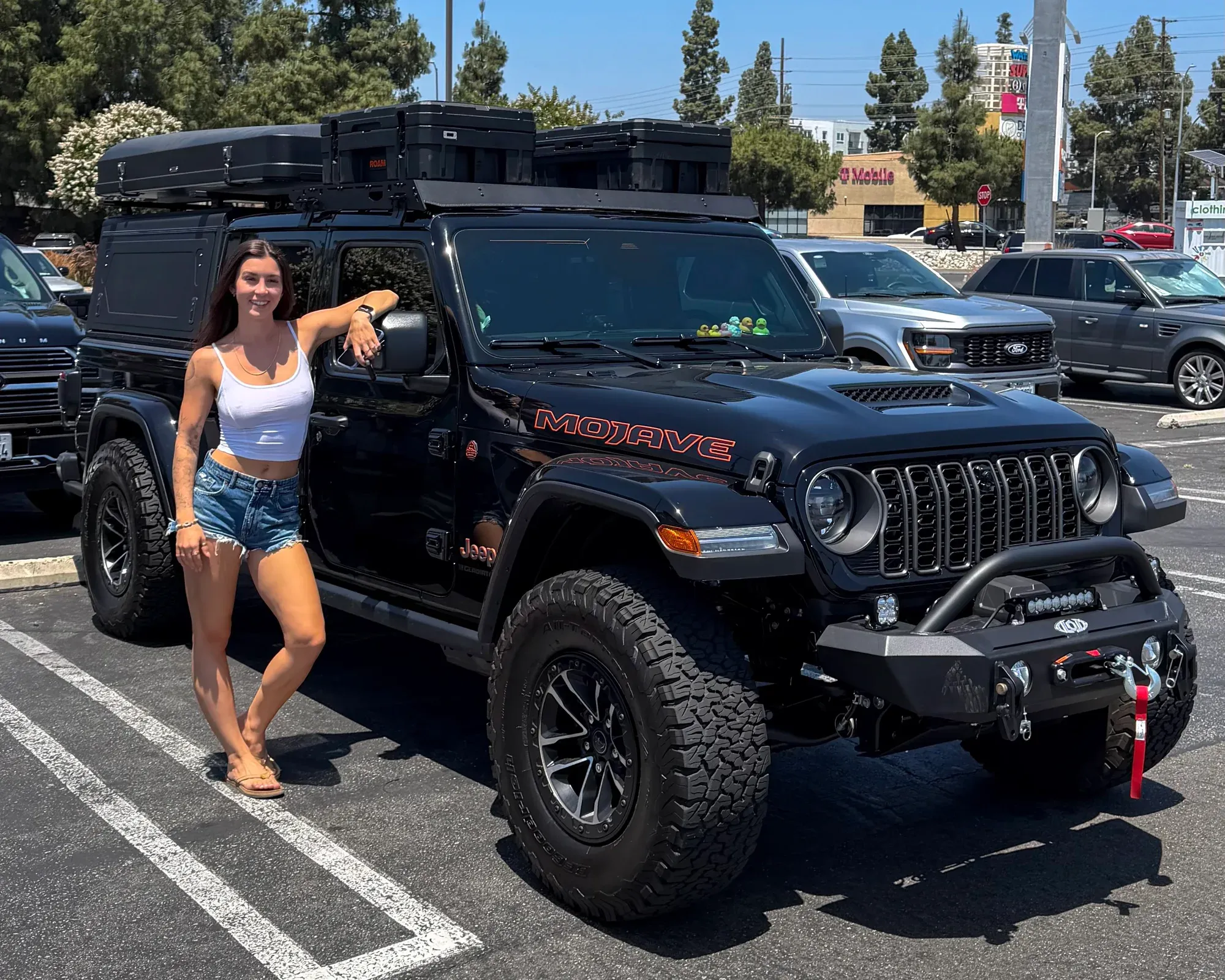 Emma beside her black Jeep Gladiator Mojave with the rooftop tent and cases on the rack